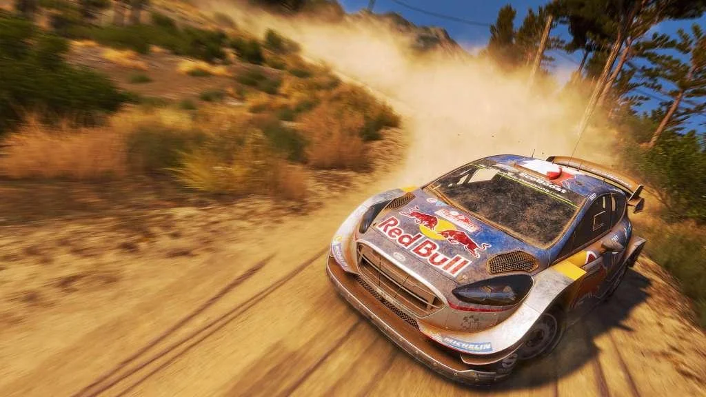 Blue-and-silver Ford with Red Bull wings drifting a sandy hairpin, dust cloud and dry yellow hills