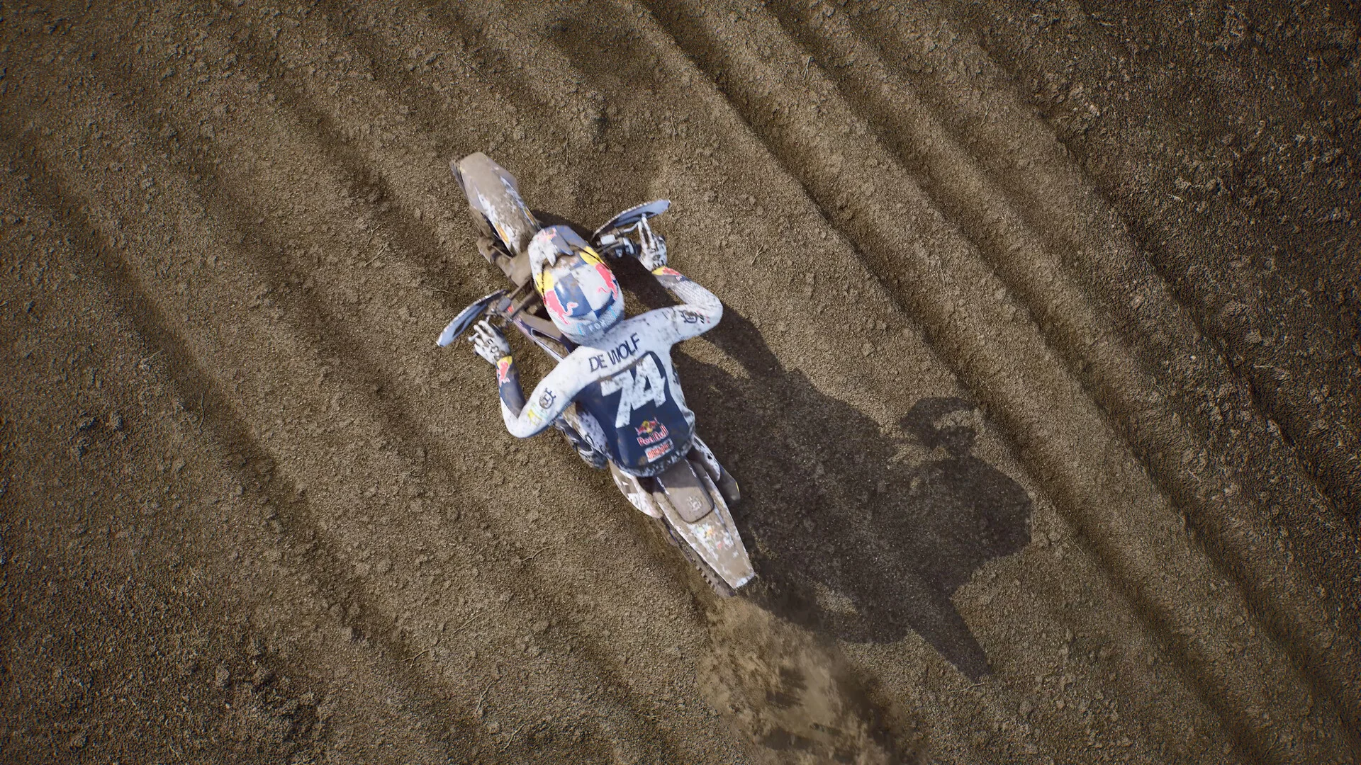 Top-down view of rider 74 De Wolf on a muddy Husqvarna carving ruts down a dirt straight