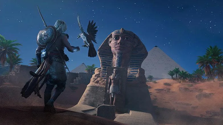 Bayek nocą unosi rękę do orła, Sfinks i piramida pod gwiazdami, palmy na wydmie z prawej