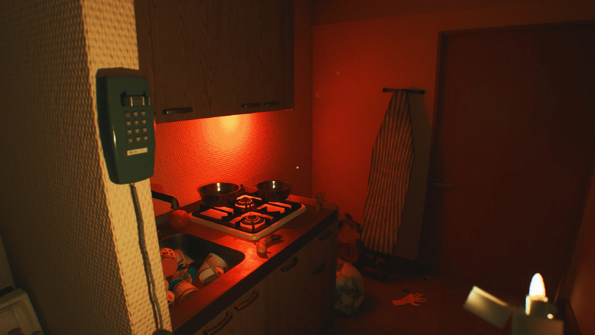 Dim kitchen with a wall intercom, pots on a gas stove, ironing board, and a lighter in the foreground
