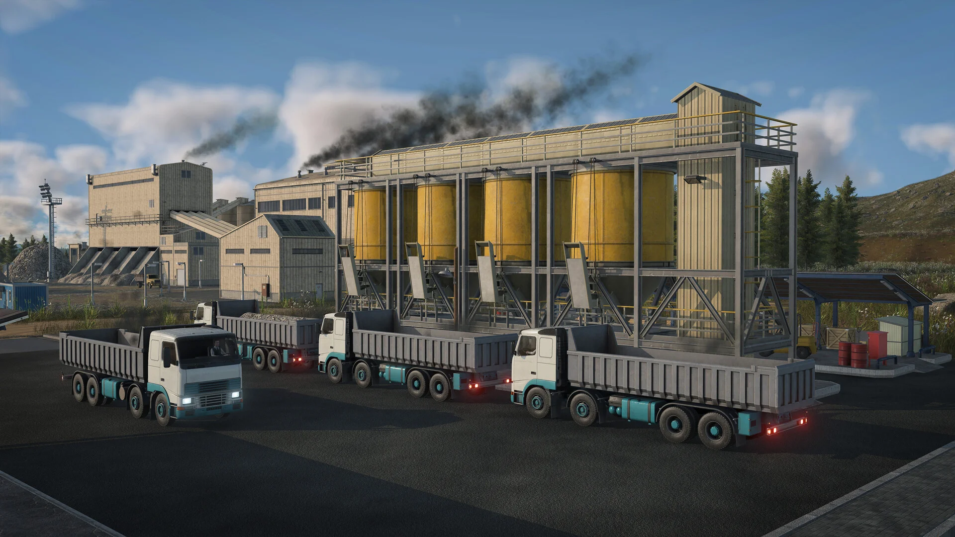 White and teal dump trucks parked beside yellow silos in a steel frame at an industrial yard