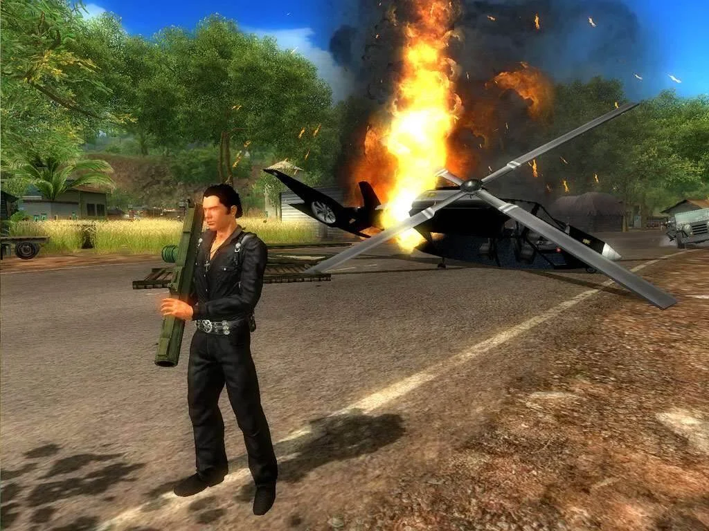 A man stands by a burning wreck in a jungle clearing.