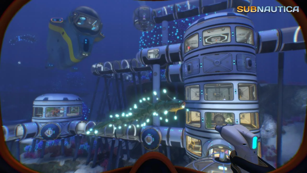 White cylindrical seafloor habitat and a yellow sub nearby, a glowing fish passing the modules
