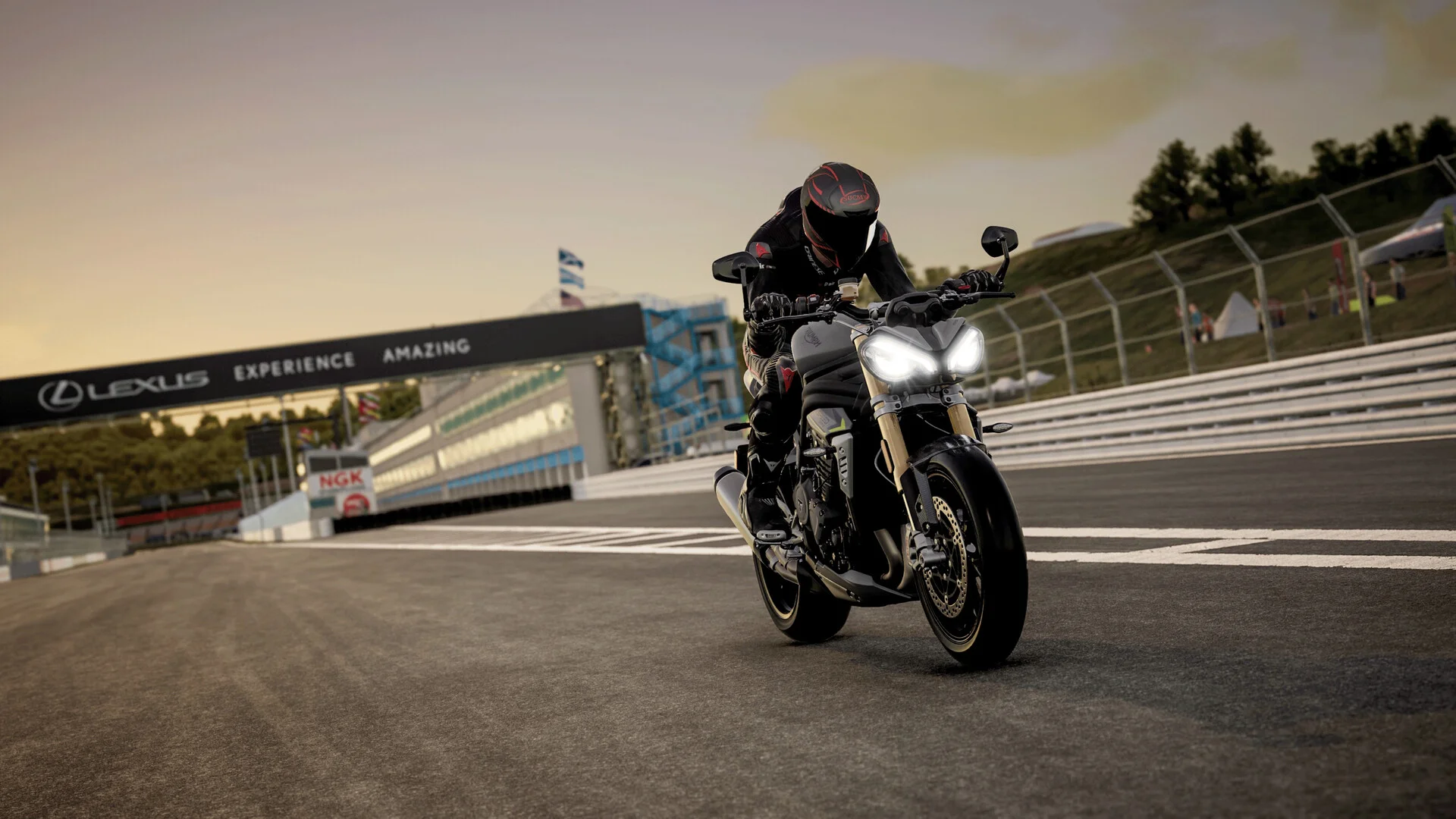 Low sun on a grey streetfighter with gold forks, rider tucked, white start-grid stripes and a Lexus EXAMAZING banner overhead