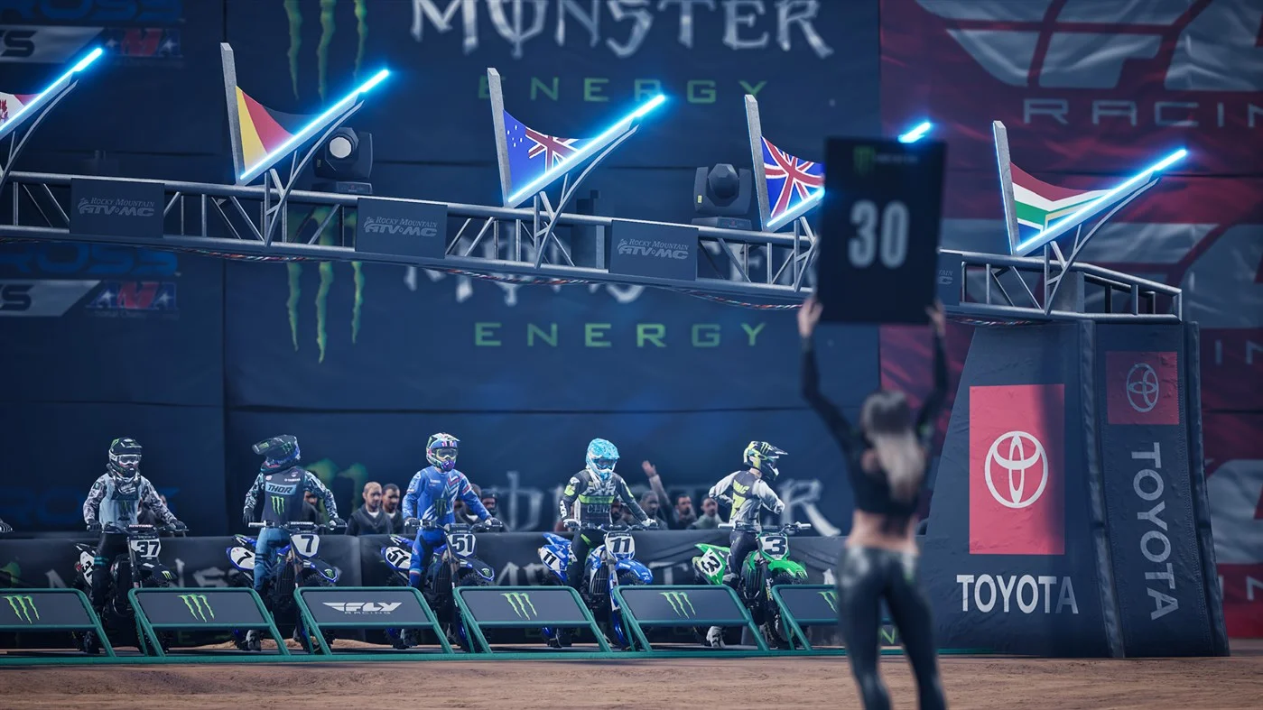 Five bikes on the gate while a 30 board is held under Monster Energy lights