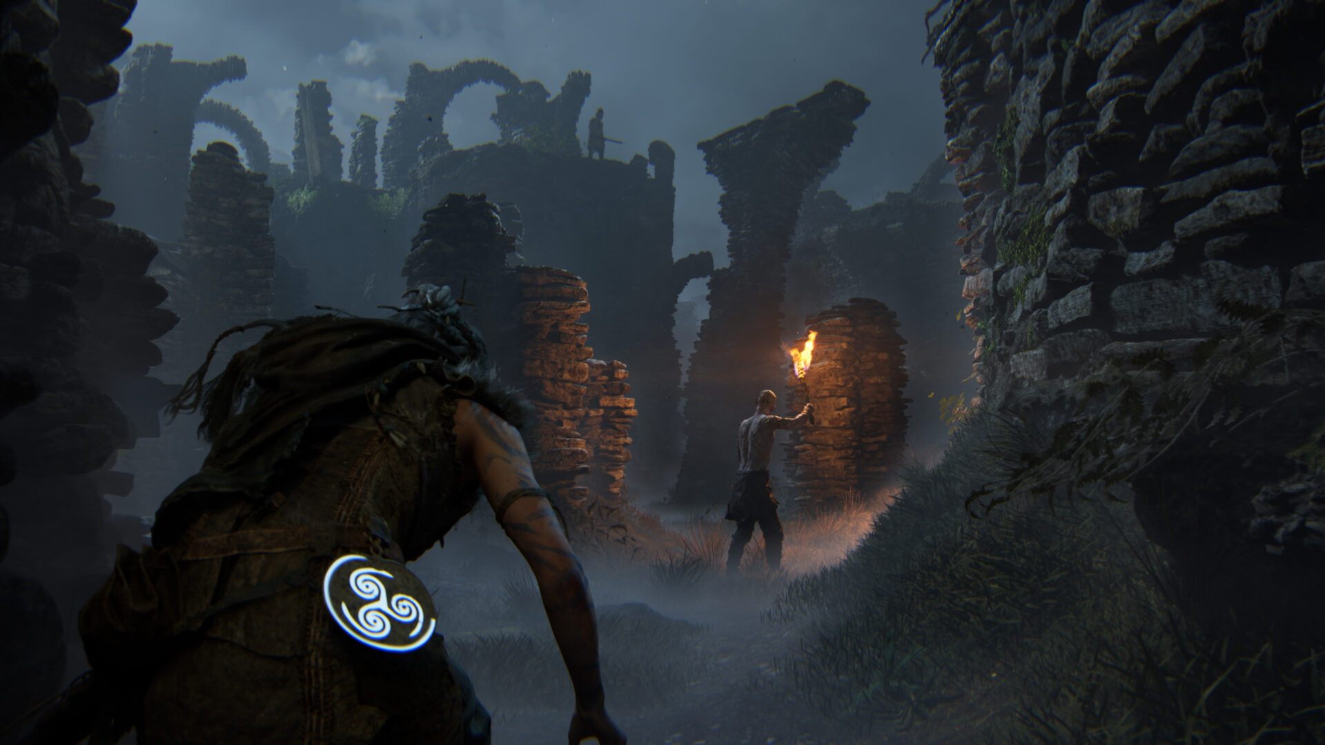 Senua stealth gameplay showing the warrior crouched in stone ruins while an enemy holds a torch ahead