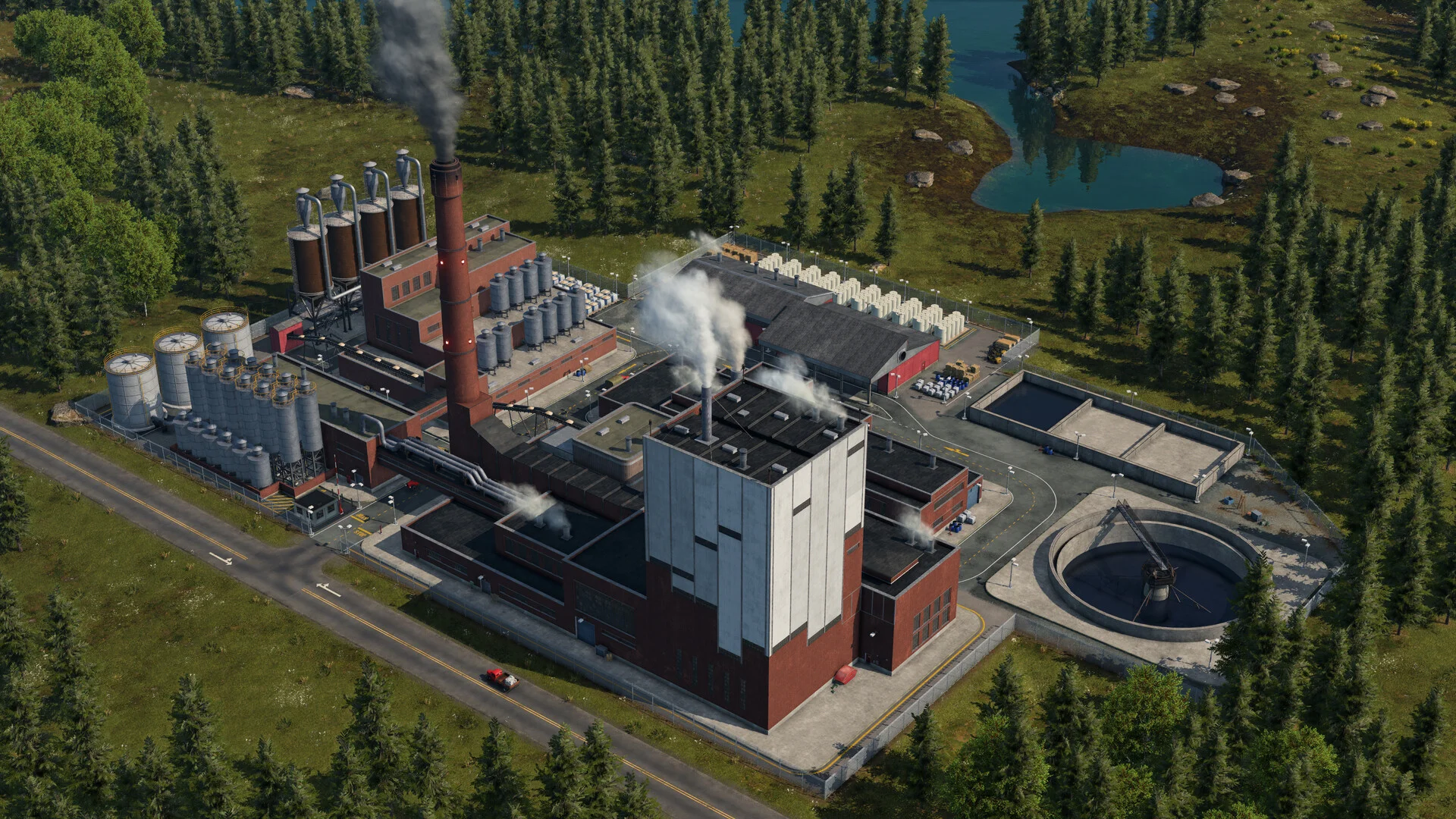 Aerial brick factory with a tall chimney, silos and a round tank among pines, a road and a pond