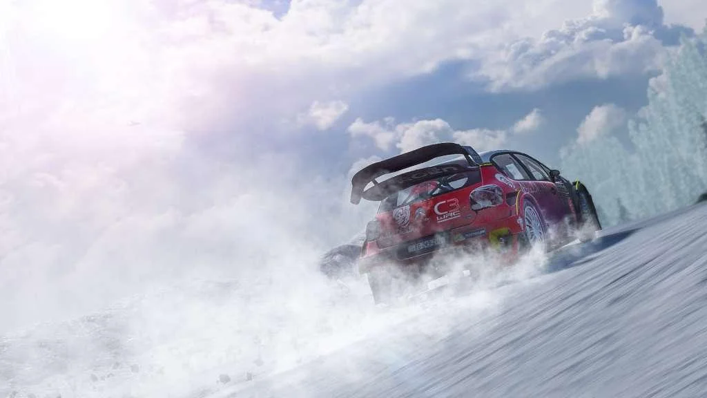 Rear of a red Citroën C3 WRC throwing a white spray on packed snow, wing high, forest and bright sky