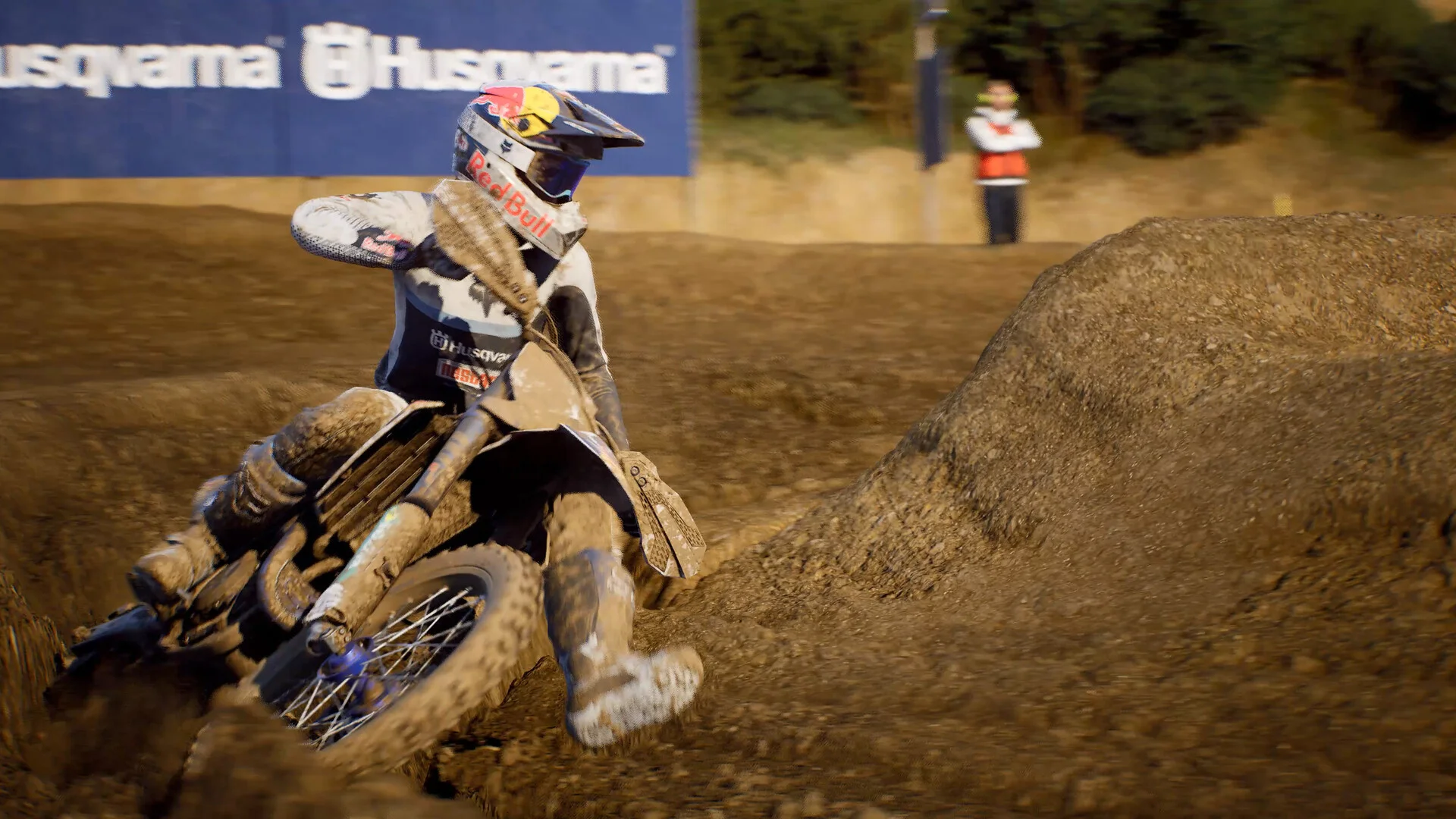Mud-caked Husqvarna rider in a Red Bull helmet leans through a rutted berm with a Husqvarna banner behind