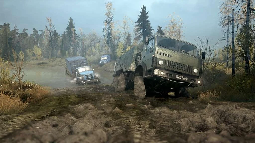 Green cab climbing a mud bank while a blue truck tows a trailer through a forest pond
