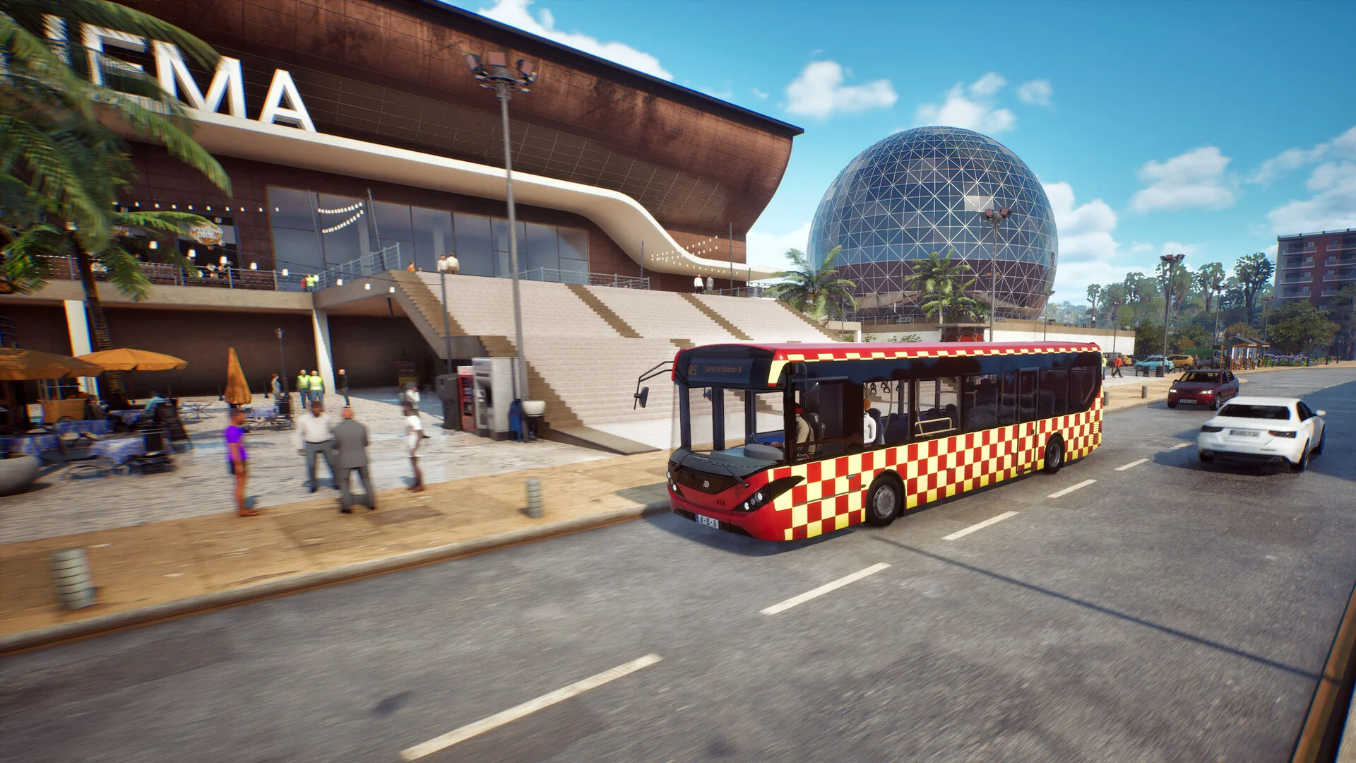A red-and-yellow checked city bus passing a cinema plaza and the glass globe landmark