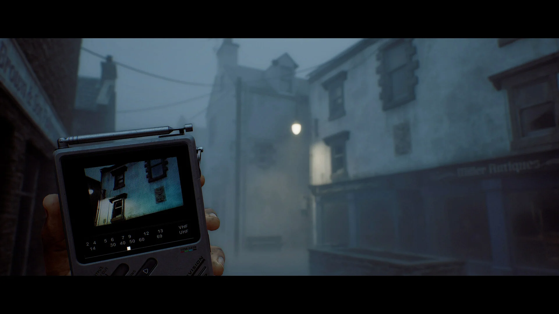 A hand holds the CRTV pocket television toward foggy stone buildings
