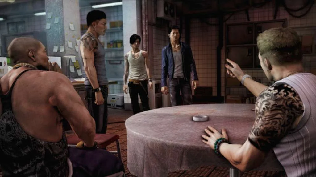 Kitchen back room: a bald man in a tank sits left, a tattooed man at a round table points, two standing men and a woman in a white tank wait by tiled walls