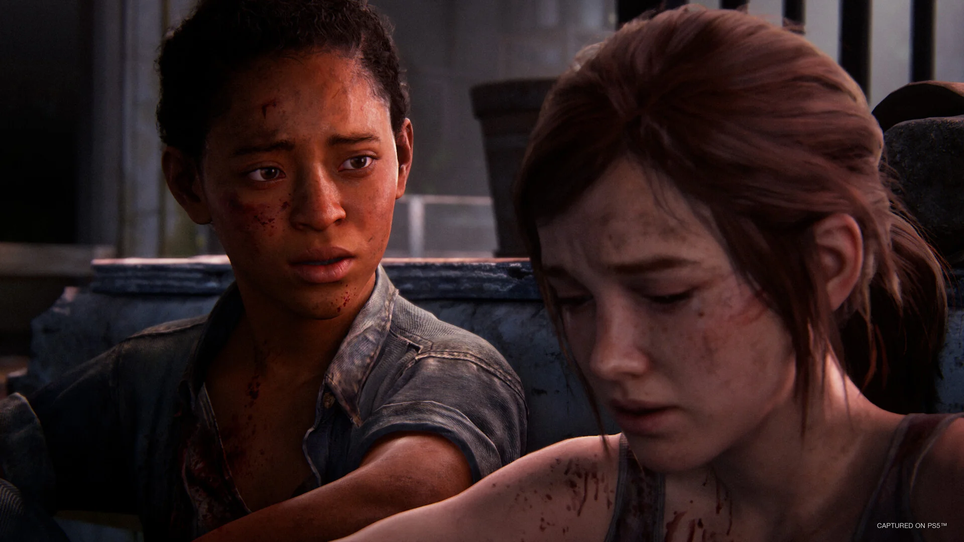 Close view of Ellie beside a bloodied young woman, both seated in worn clothes