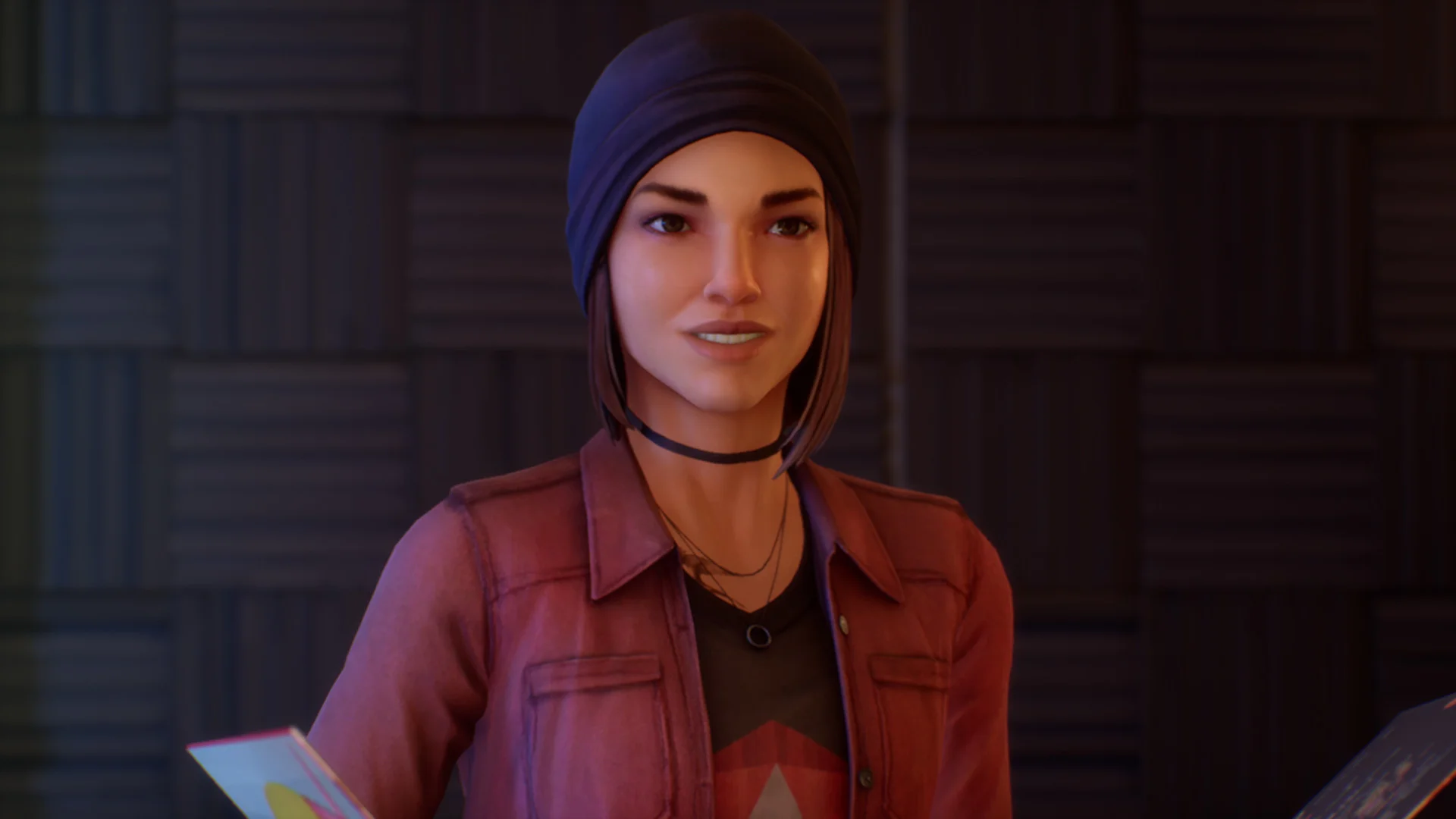 Alex in a beanie and red jacket in a dark room.
