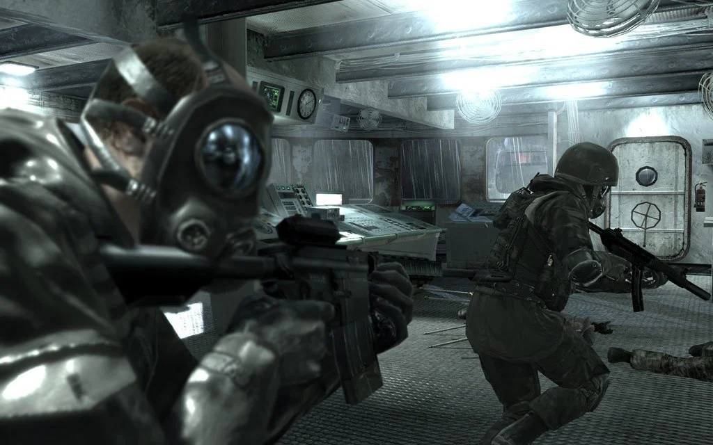Gas-masked soldier in a metal cabin aiming a carbine while a helmeted teammate advances past consoles