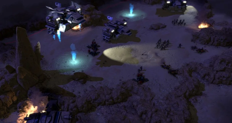 Dropships with blue thrusters hovering over a sand bowl while squads and wrecks sit under searchlights