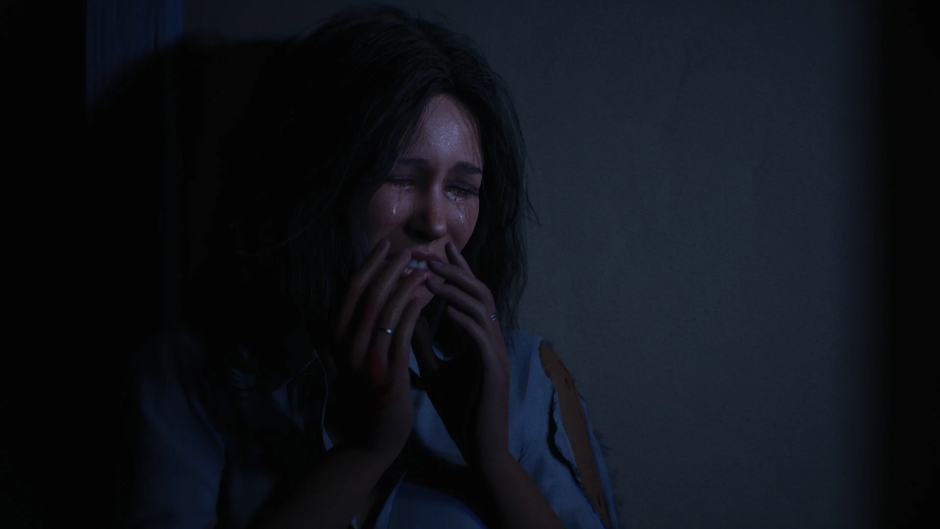 A young woman covering her mouth in tears against a dark wall