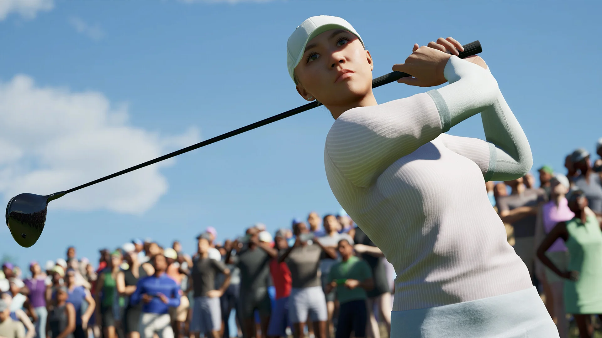 A golfer in a pale ribbed top finishing a driver swing before a crowded gallery