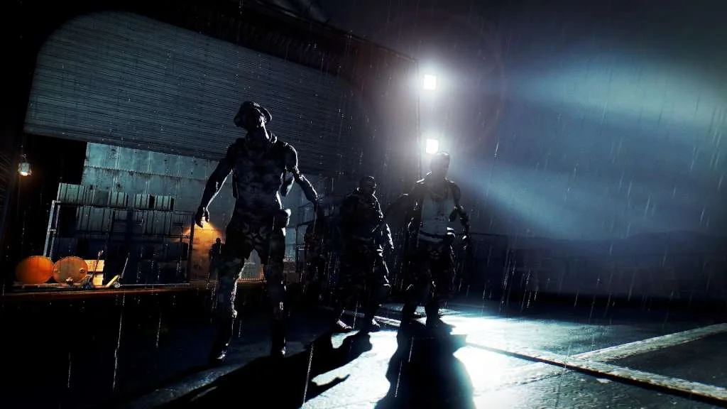 Rainy warehouse dock at night with three zombie silhouettes under harsh spotlights and wet reflections