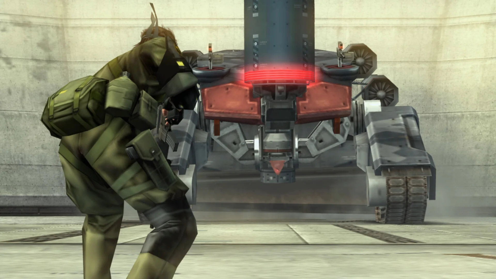 Green sneaking suit aiming at a tracked mech with a glowing red core in a concrete hangar