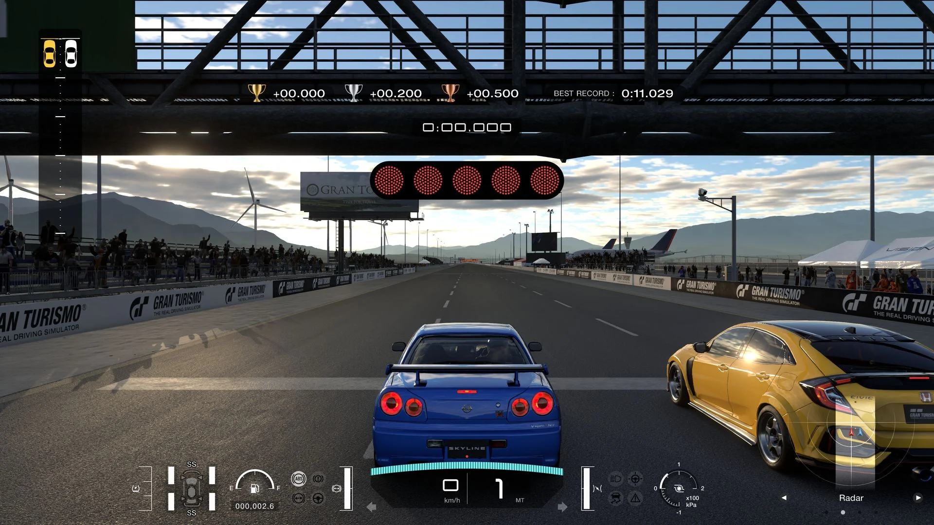 Rear view of a blue car under a gantry with position lights.