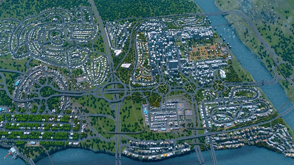 River-split city seen from above with ring roads, cul-de-sacs, and a wind farm