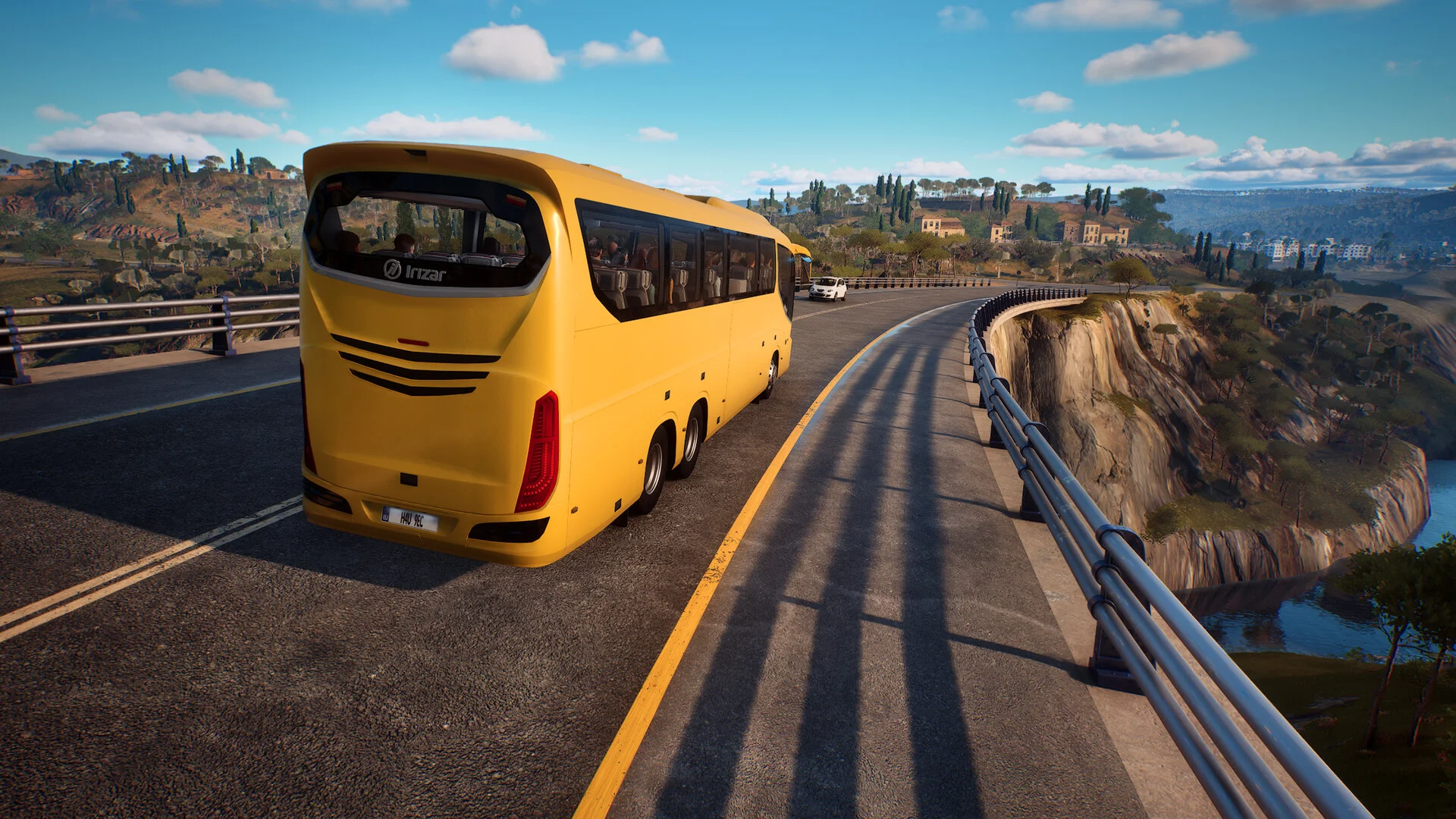 A yellow Irizar coach on a cliffside highway with hills and water below the guardrail