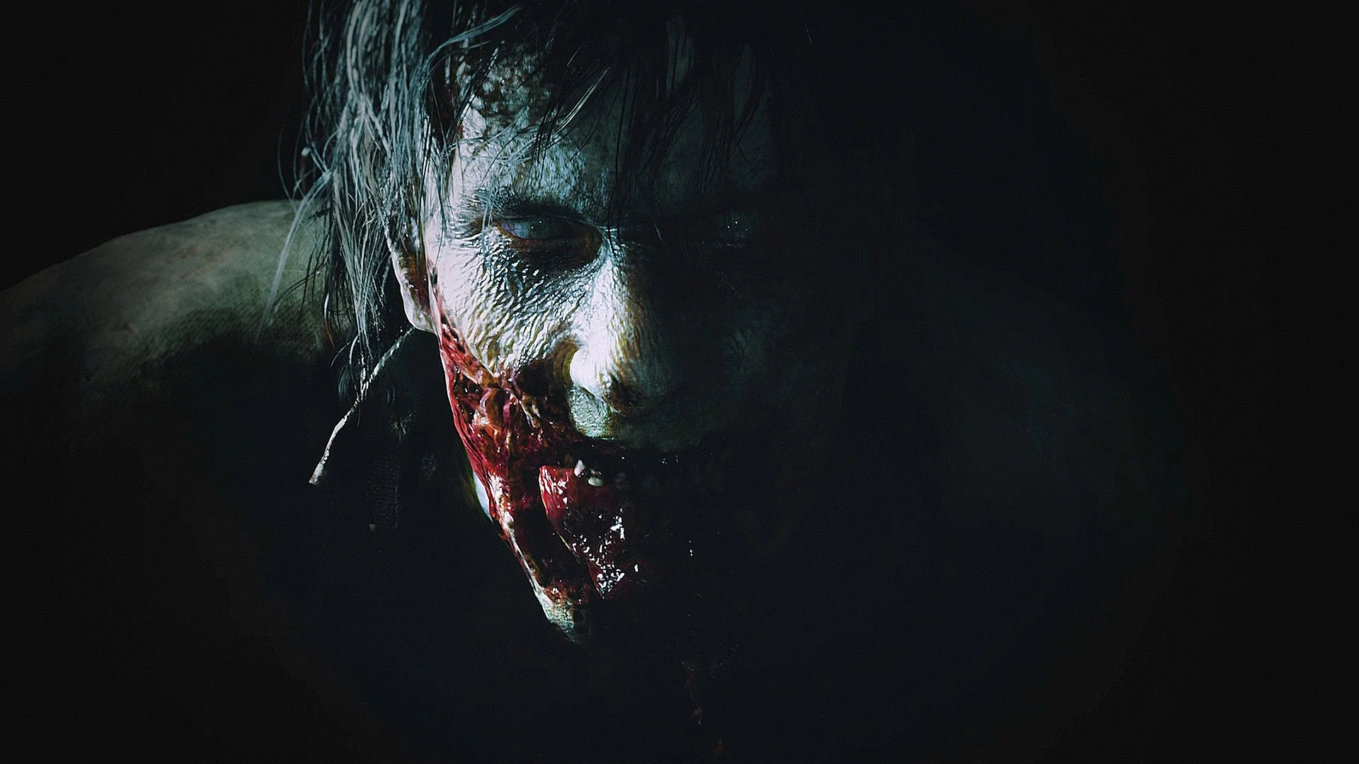 Close-up of a rotting face with a torn cheek and dark hair against black